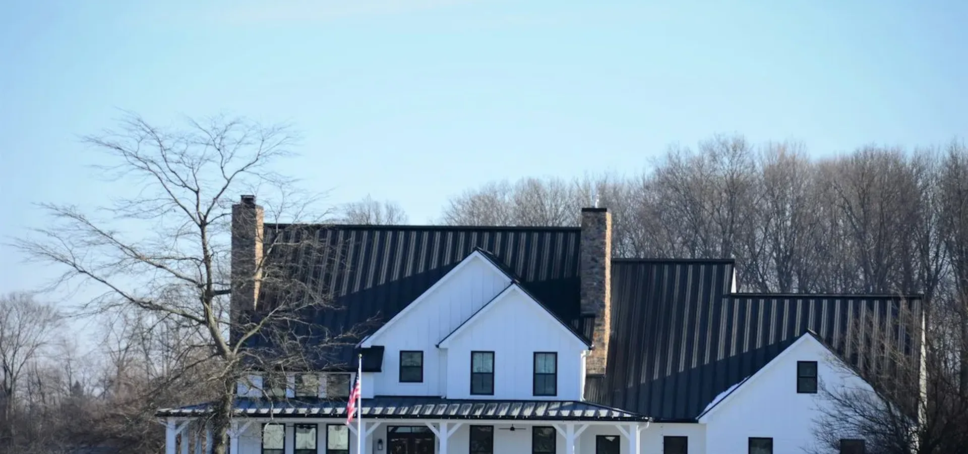 Black 6-inch seamless K-style aluminum gutters and downspouts lining a white farmhouse with a black metal roof